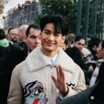 Smiling man among a crowd on a lively Paris street, capturing modern fashion and public event atmosphere.