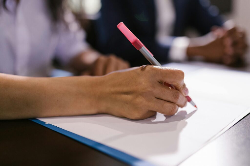 Detailed close-up of a person writing on paper with a pen in an office setting.